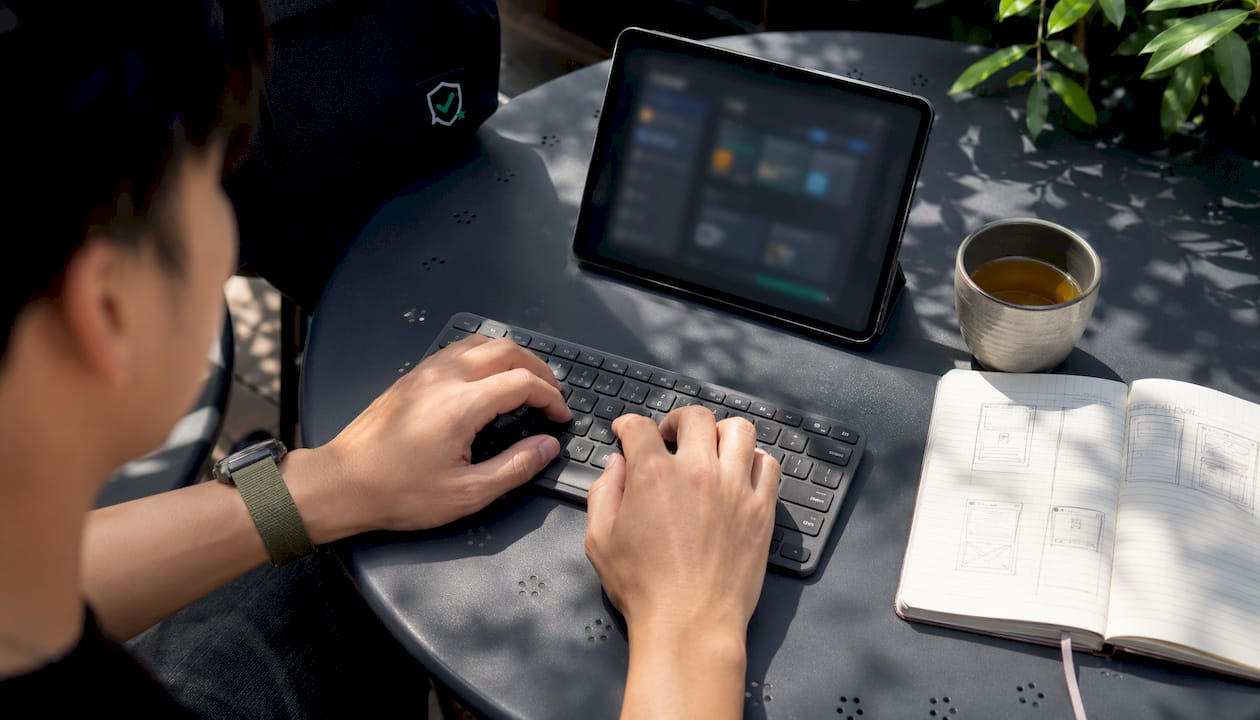 Detailopname van handen die typen op een toetsenbord, terwijl op een tablet een webshop te zien is.